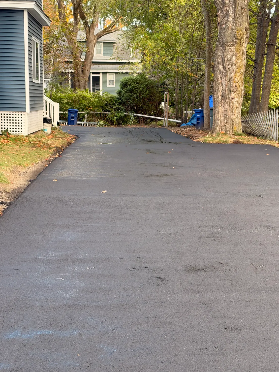 Fresh driveway sealcoat next to a blue house