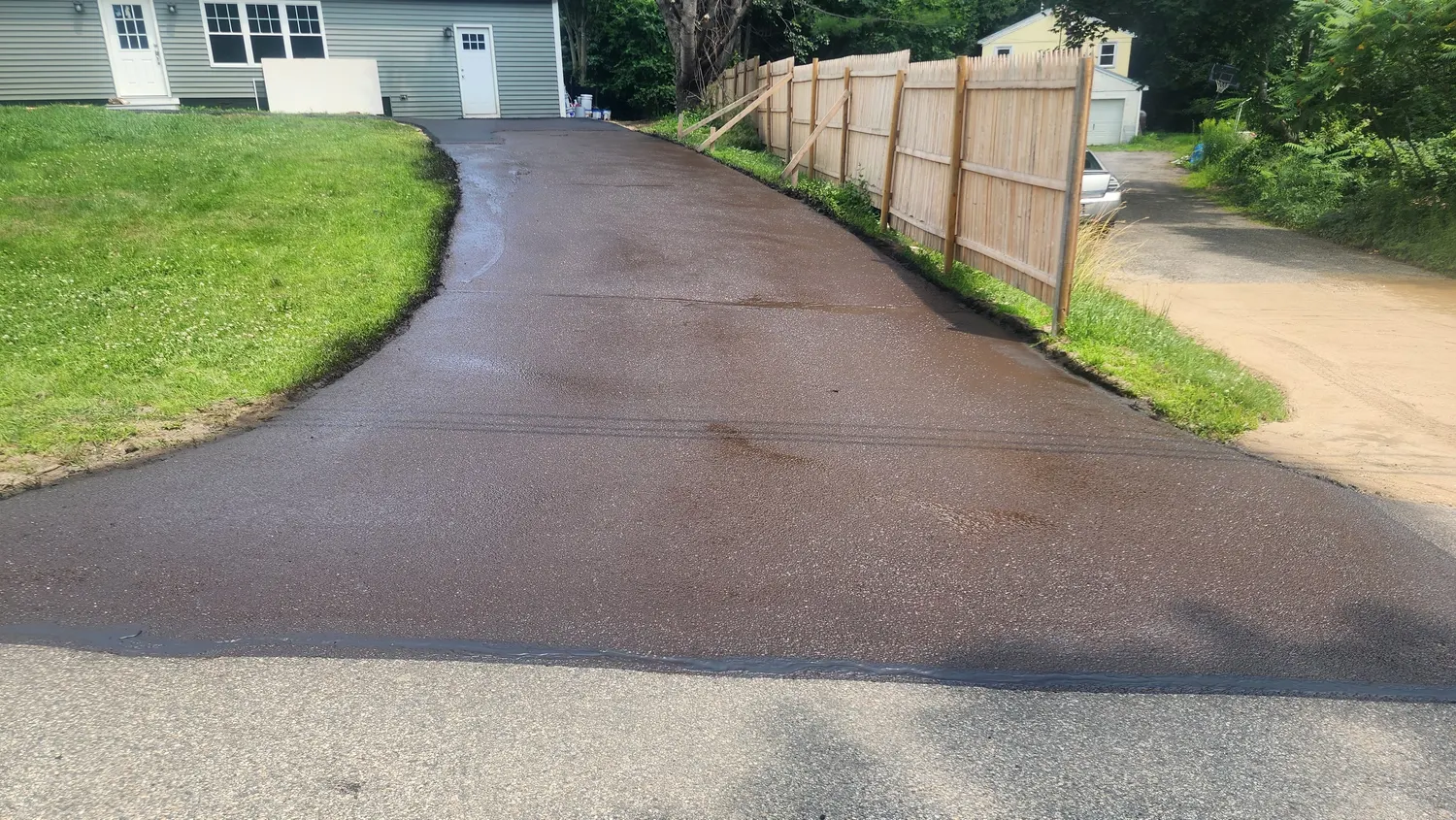 Long sealcoated driveway beside a fence in summer